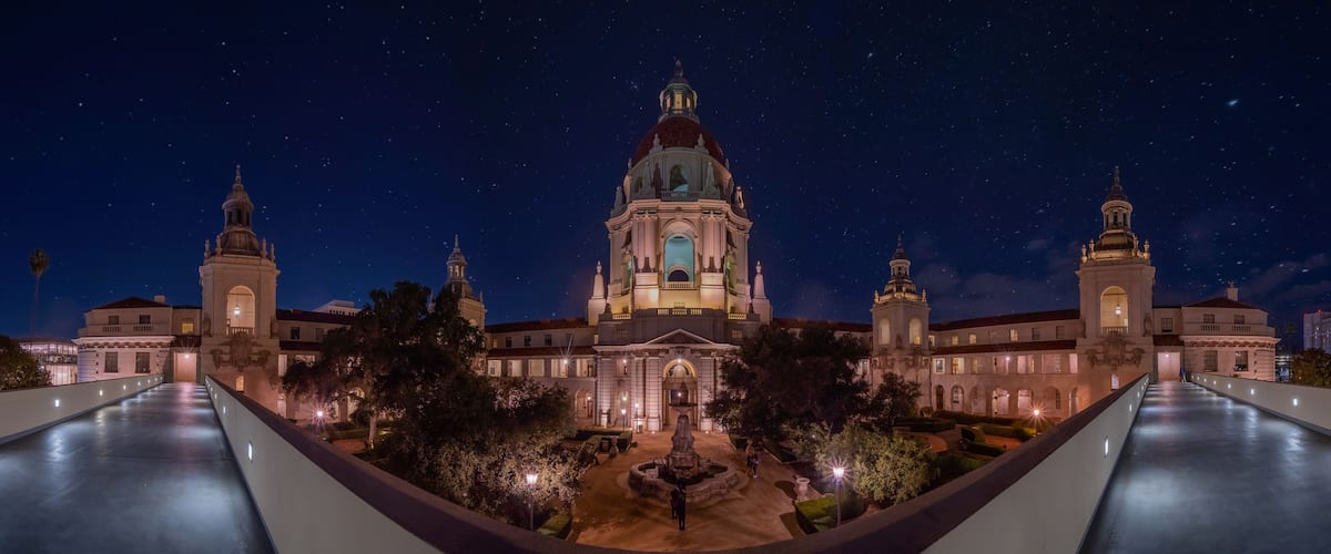 A grand building with a central dome and two smaller domes, surrounded by a well-lit courtyard and a starry night sky.