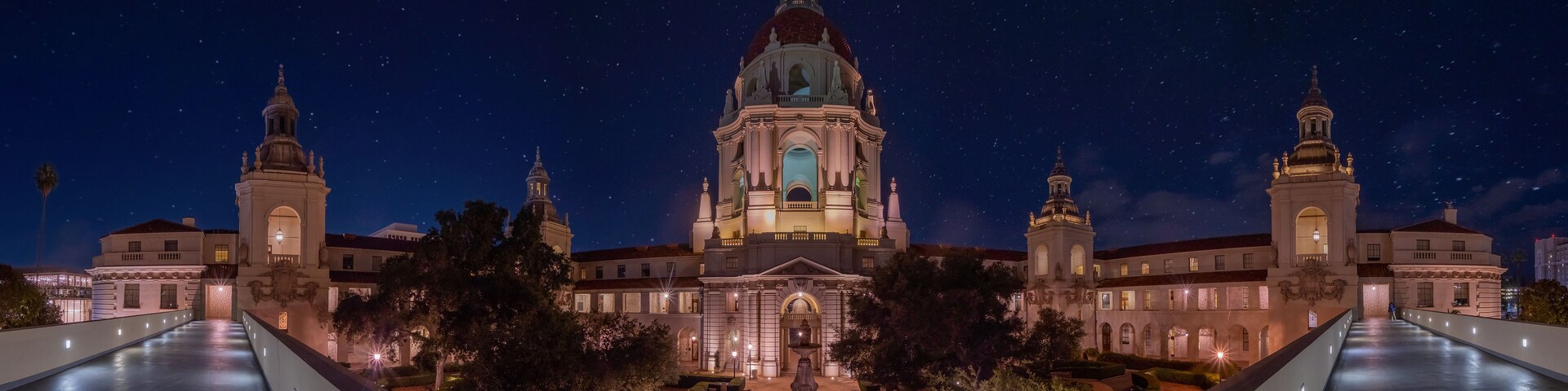 A grand building with a central dome and two smaller domes, surrounded by a well-lit courtyard and a starry night sky.