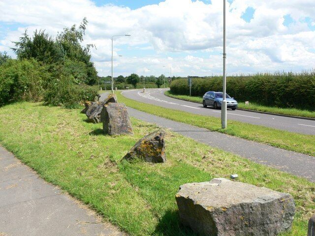 A road with large rocks on the side, a car on the road, and a grassy area with bushes.
