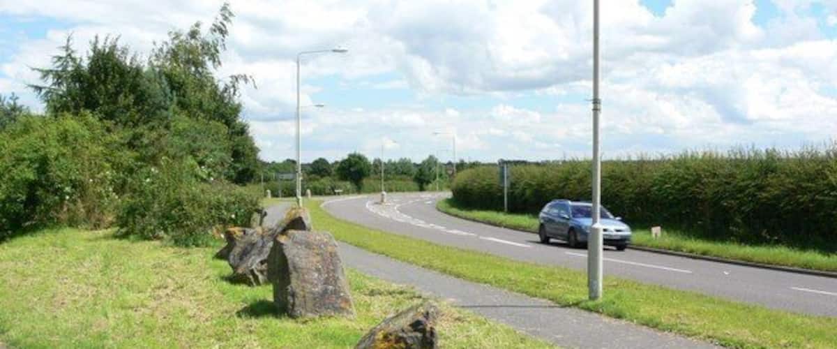 A road with large rocks on the side, a car on the road, and a grassy area with bushes.