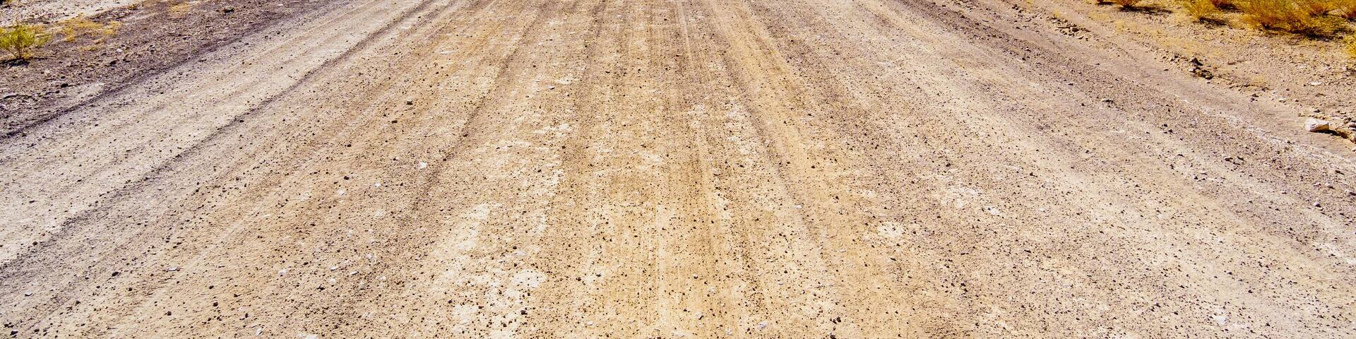 A long and straight gravel road in the semi desert landscape near Crystal Springs and Area 51 in the desolate land of the Nevada desert in the United States