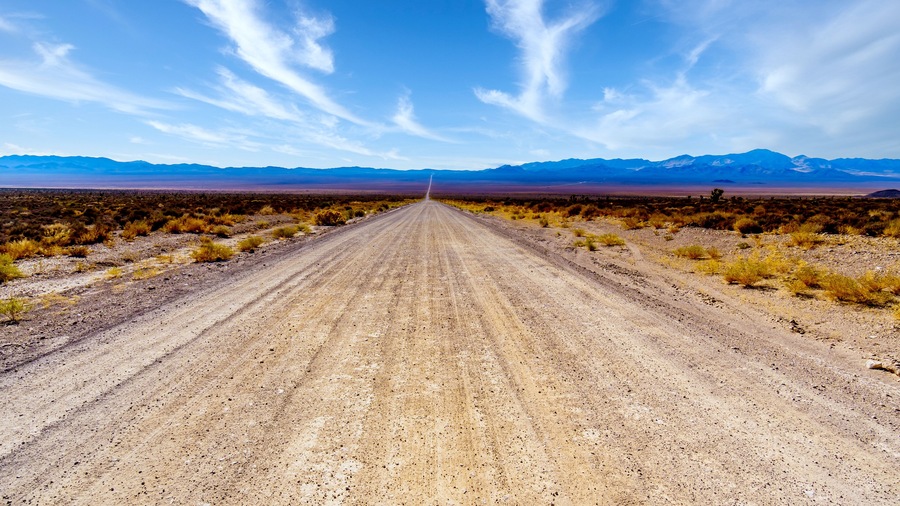 A long and straight gravel road in the semi desert landscape near Crystal Springs and Area 51 in the desolate land of the Nevada desert in the United States