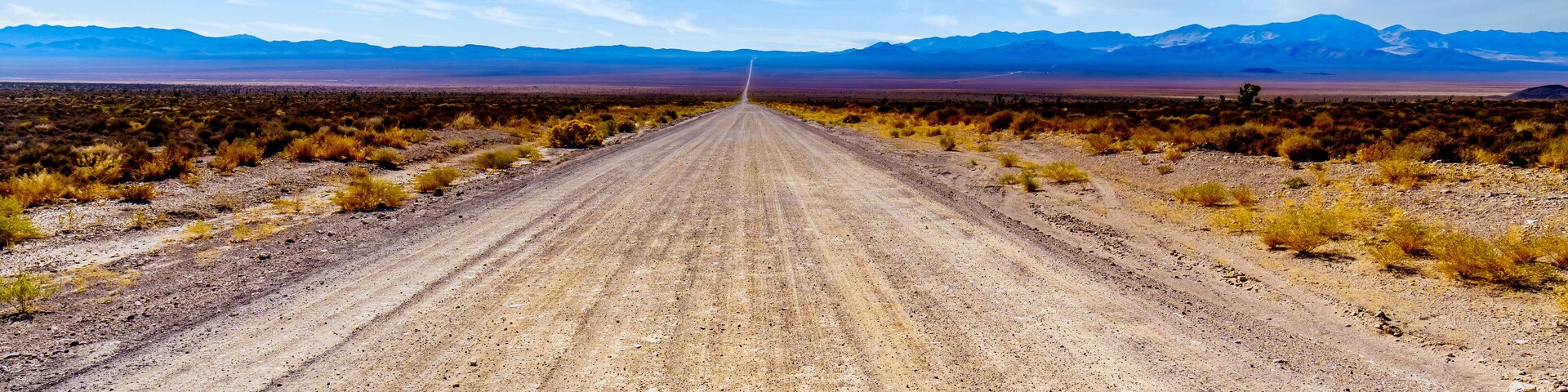 A long and straight gravel road in the semi desert landscape near Crystal Springs and Area 51 in the desolate land of the Nevada desert in the United States