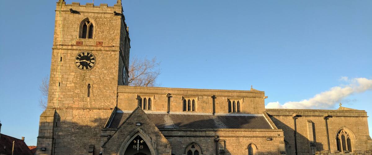 A historic church with a clock tower, arched windows, and a well-maintained lawn.