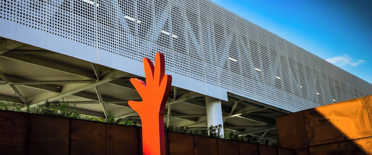 A modern building with a perforated metal facade and a large orange hand sculpture.