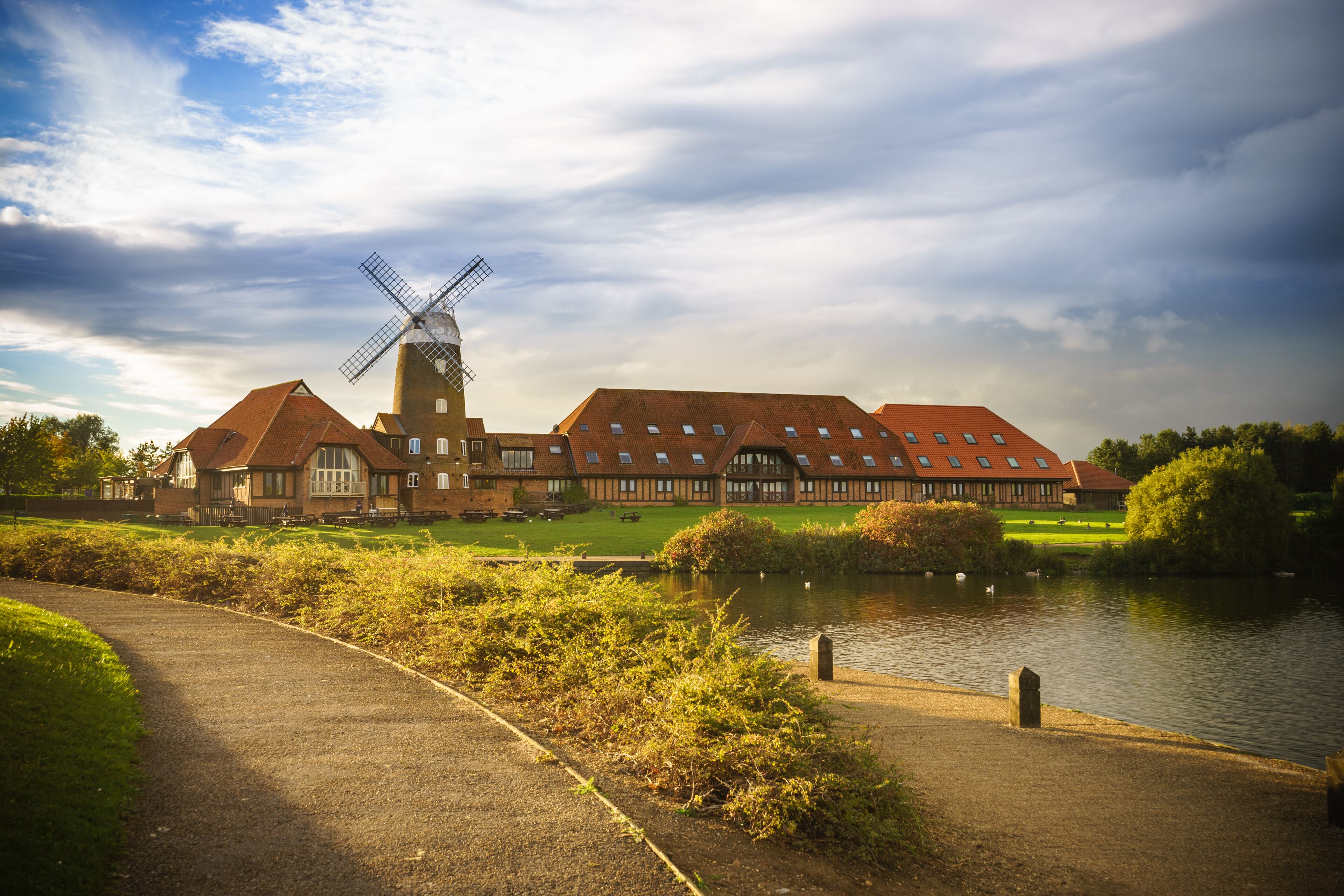 A windmill, a pond, and a building with a red roof.