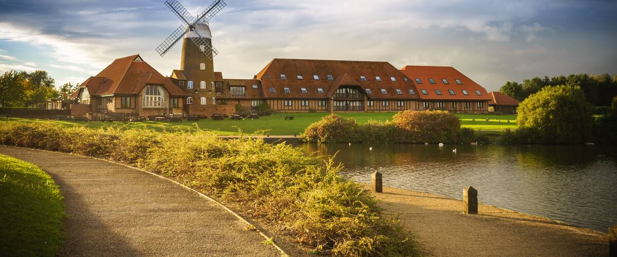 A windmill, a pond, and a building with a red roof.