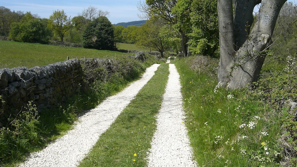 A gravel path flanked by stone walls and trees in a rural landscape.