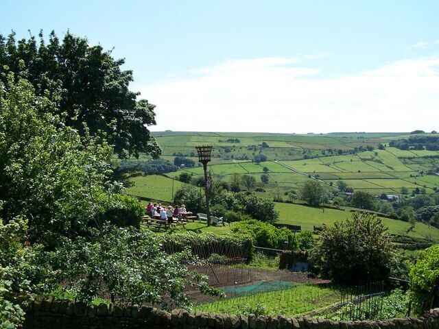 View from Towngate, High Bradfield Allotments and Diners at the Old Horns Inn are in the foreground, as is the Jubilee Fire Brazier which is lit on special occasions. The road in the background is Mill Lee Road which runs up from Low Bradfield towards Ughill Height.