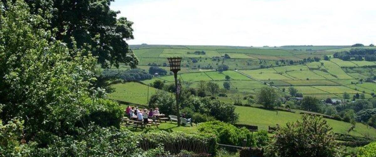 View from Towngate, High Bradfield Allotments and Diners at the Old Horns Inn are in the foreground, as is the Jubilee Fire Brazier which is lit on special occasions. The road in the background is Mill Lee Road which runs up from Low Bradfield towards Ughill Height.