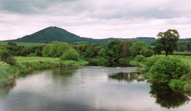 A calm river with a mountain in the background and lush greenery on the banks.