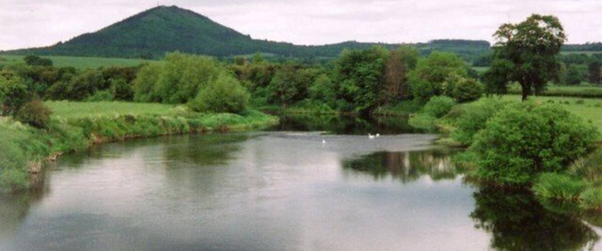 A calm river with a mountain in the background and lush greenery on the banks.