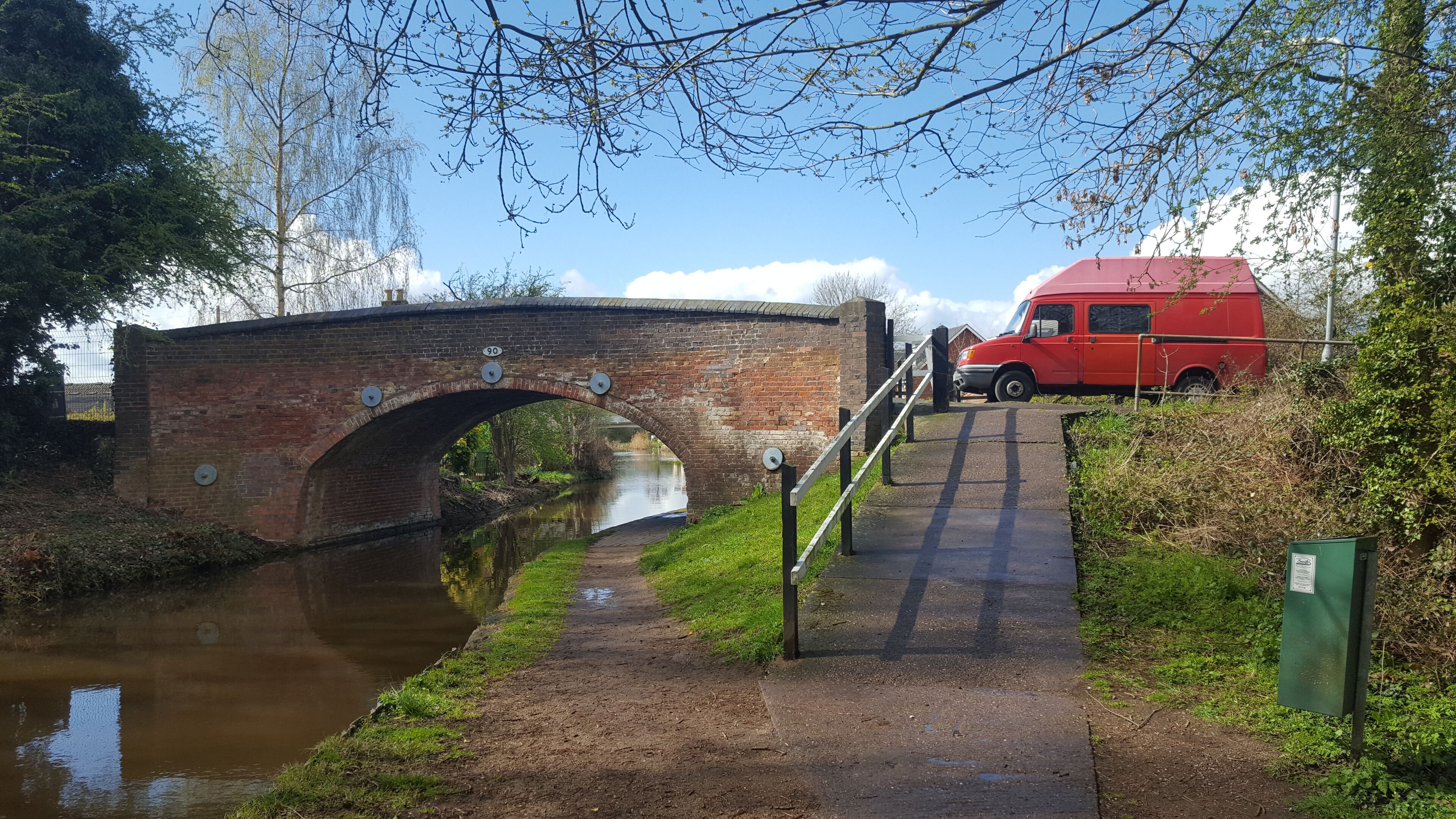 A brick bridge over a canal with a red van parked nearby.