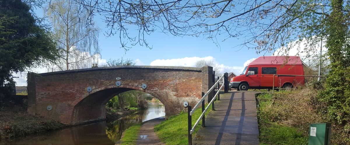 A brick bridge over a canal with a red van parked nearby.