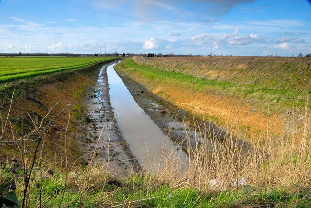 A narrow water channel in a rural landscape with green fields on either side.