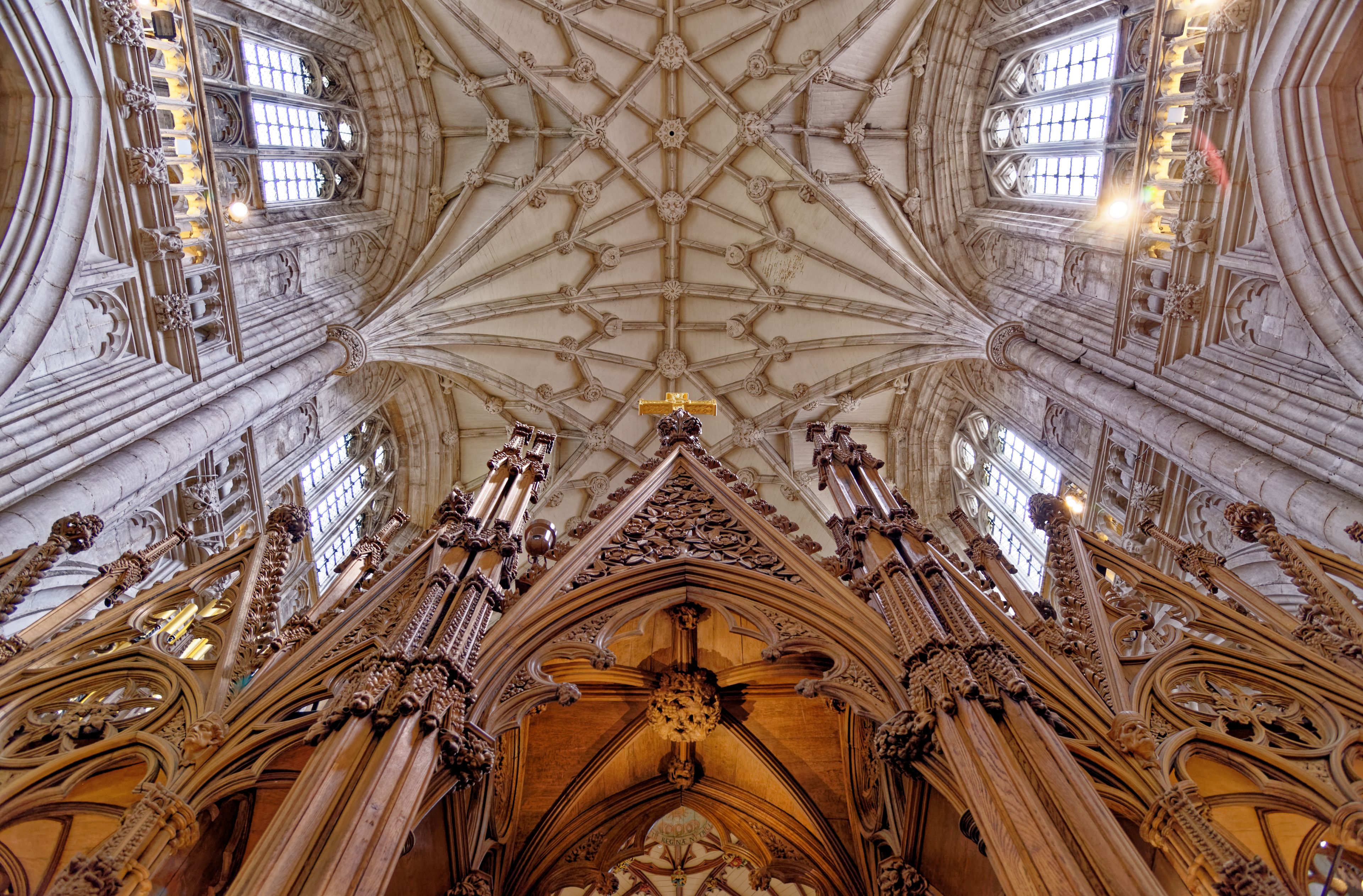 A cathedral's ornate ceiling with intricate wood carvings and a central cross.