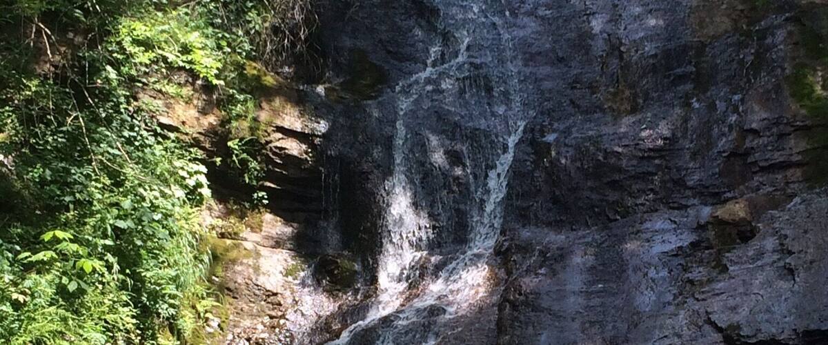 A waterfall cascading over a rocky cliff surrounded by lush greenery.