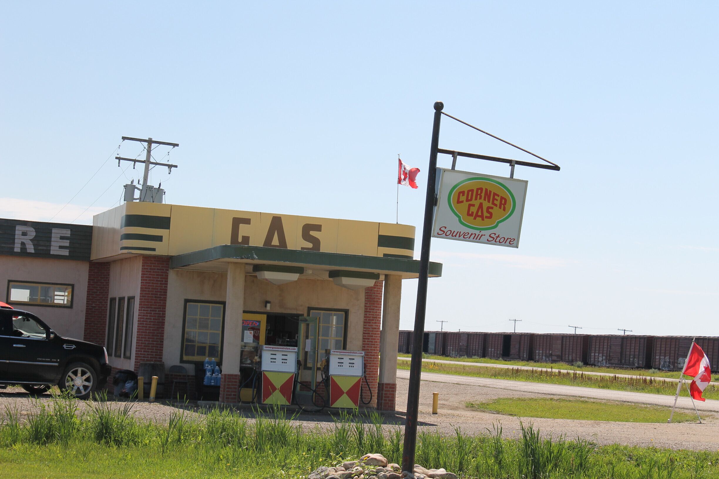 A gas station named 'CORNER CAS' with a Canadian flag, a black truck parked in front, and a fence in the background.