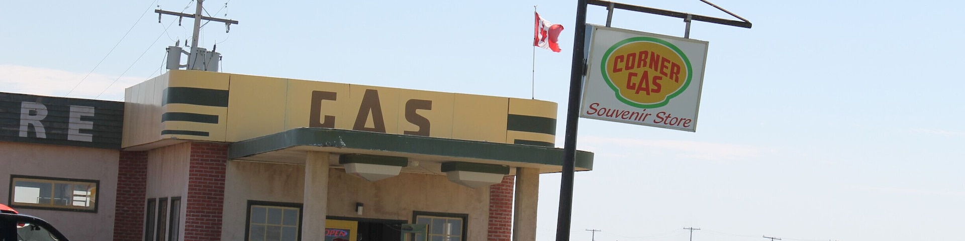 A gas station named 'CORNER CAS' with a Canadian flag, a black truck parked in front, and a fence in the background.