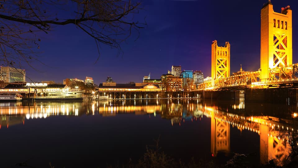 A nighttime cityscape with illuminated buildings and a river reflecting the lights.