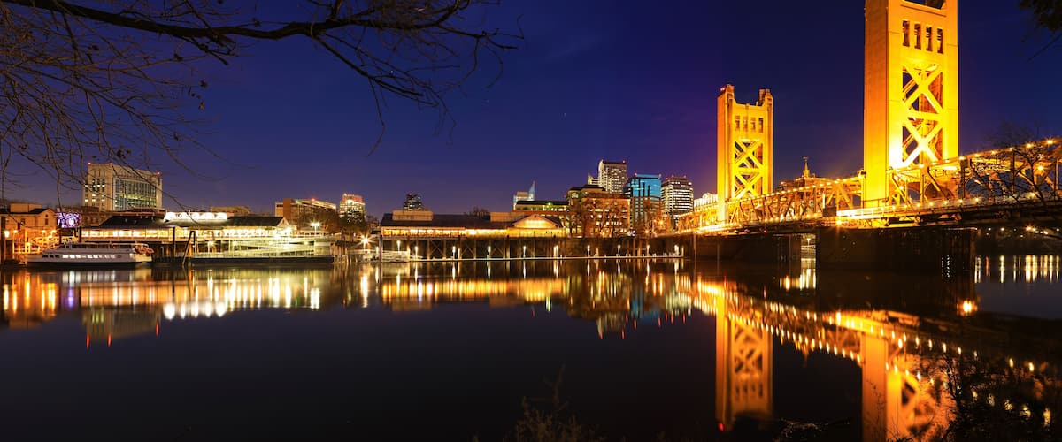 A nighttime cityscape with illuminated buildings and a river reflecting the lights.