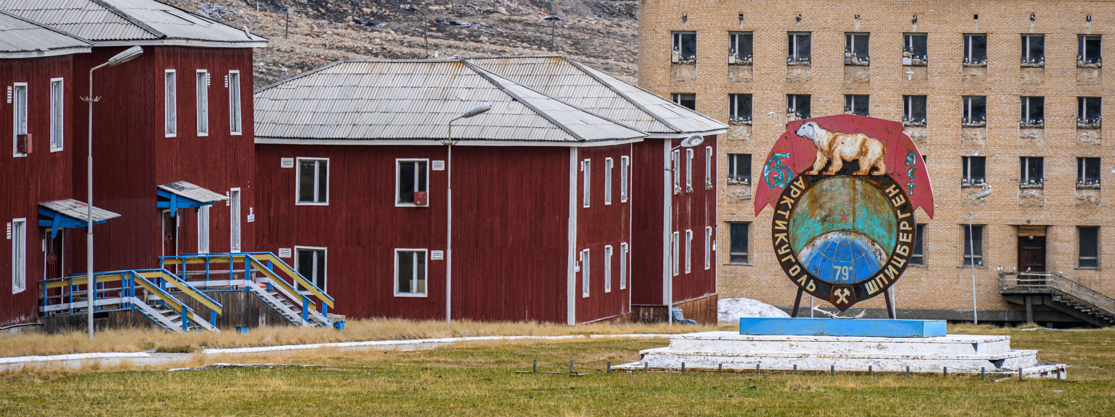 A red barn with a blue staircase, a large mural of a polar bear, and a brick building in the background.