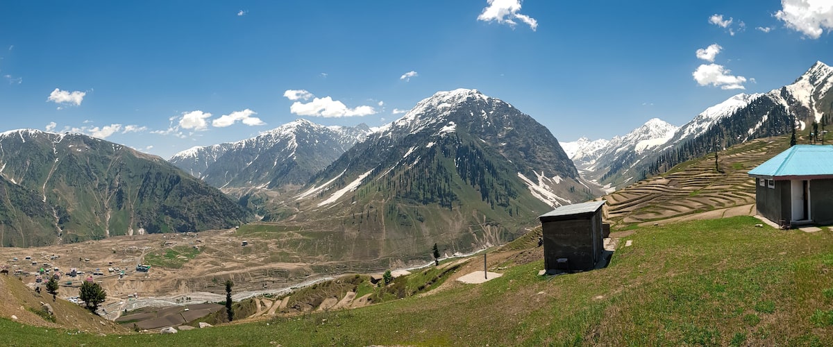 A mountainous landscape with snow-capped peaks, terraced fields, and small buildings.