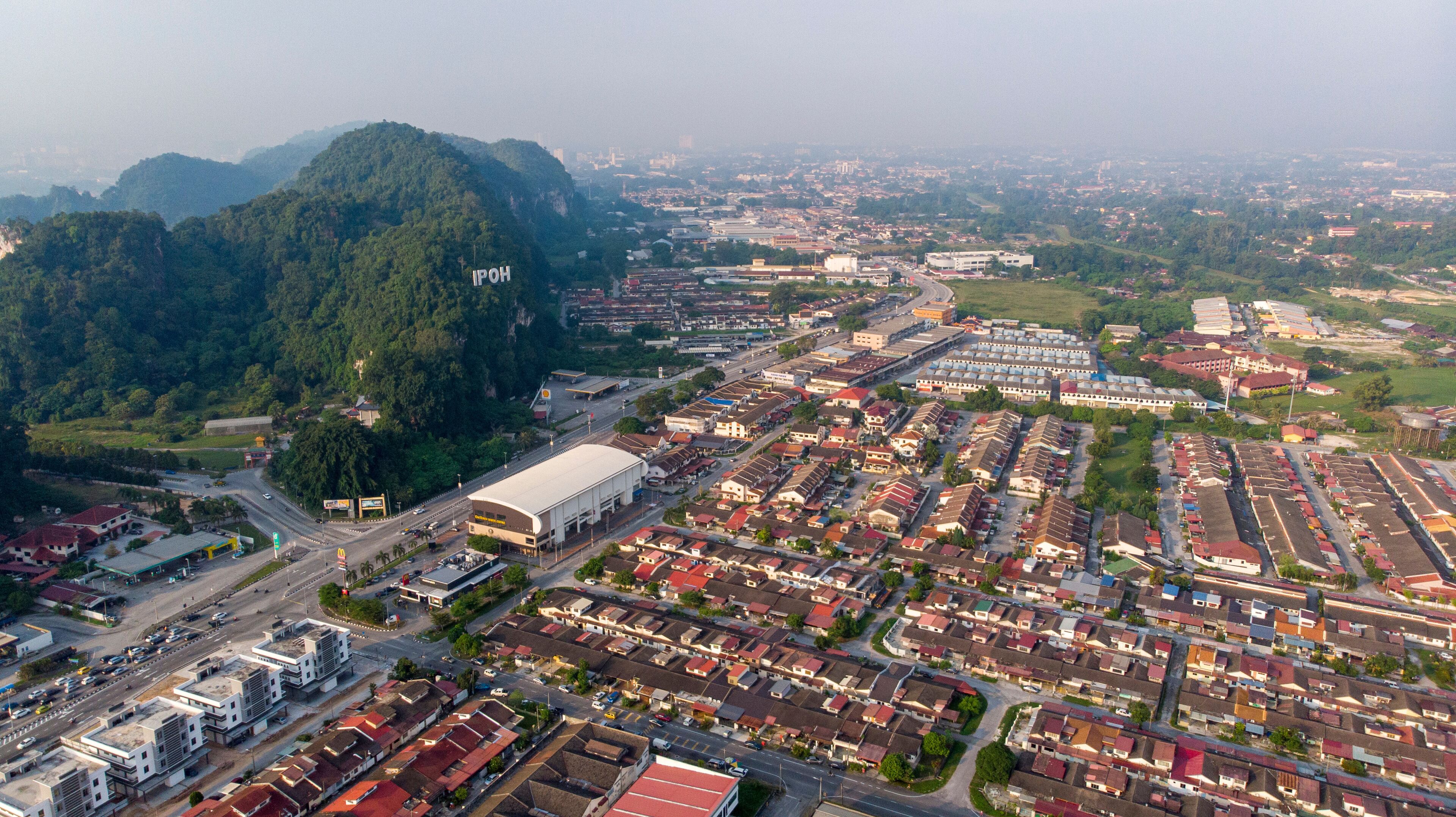 An aerial view of a city with a large industrial area, residential neighborhoods, and a prominent mountain in the background.