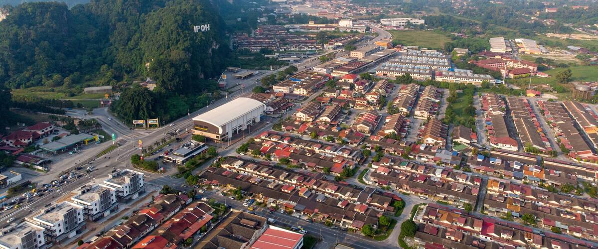 An aerial view of a city with a large industrial area, residential neighborhoods, and a prominent mountain in the background.