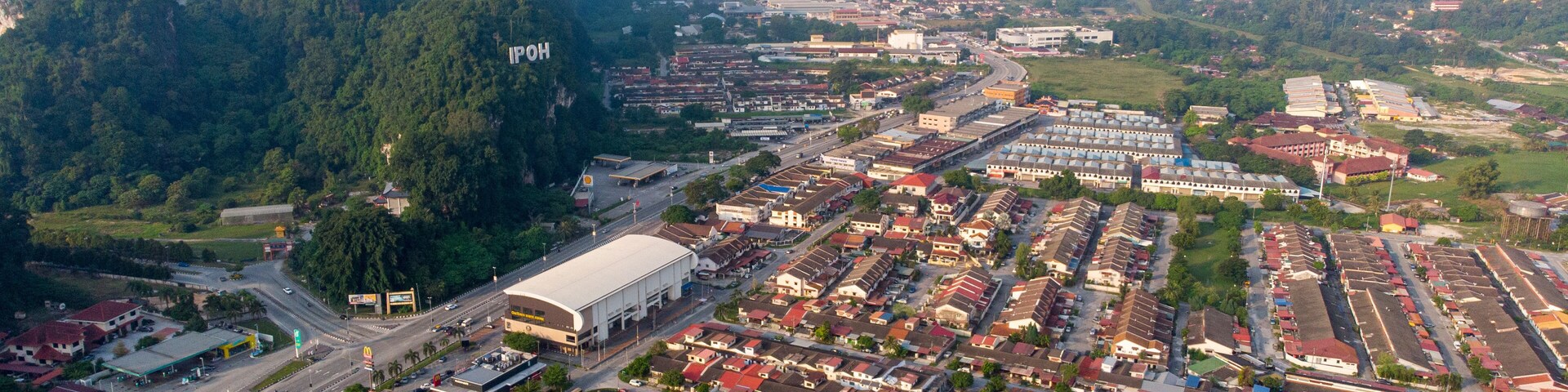 An aerial view of a city with a large industrial area, residential neighborhoods, and a prominent mountain in the background.