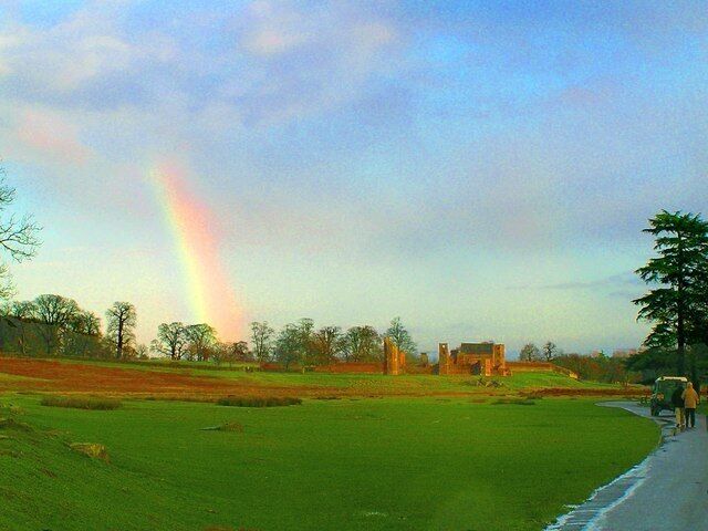 A grassy field with a rainbow, a road, and some buildings in the distance.