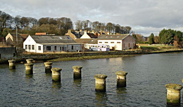 The pillars mark the position of an old railway bridge built in 1852 by Thomas Bouch who was made infamous in 1879 by the collapse of the Tay Railway Bridge which he also engineered. The railway was closed in 1969. The factory in the background is a paper mill operated by Curtis Fine Papers.