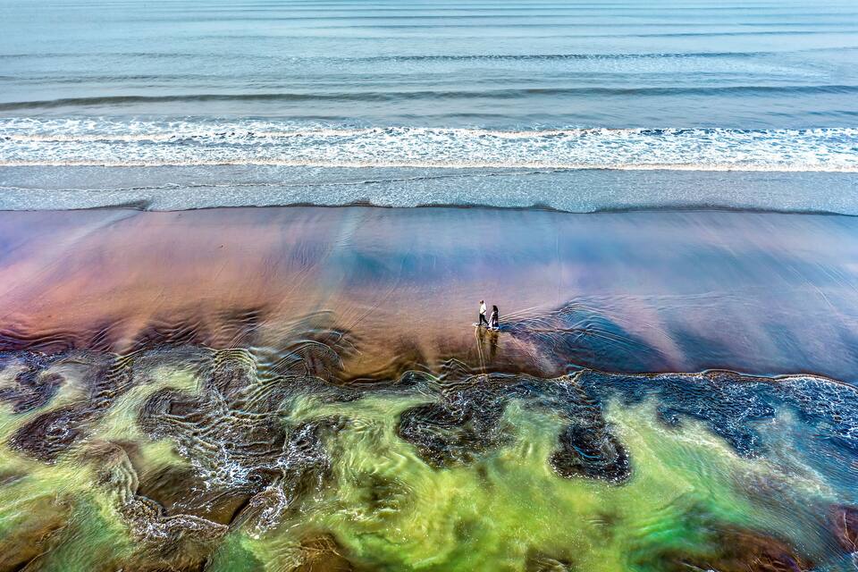 A beach with a unique color pattern in the sand and water.