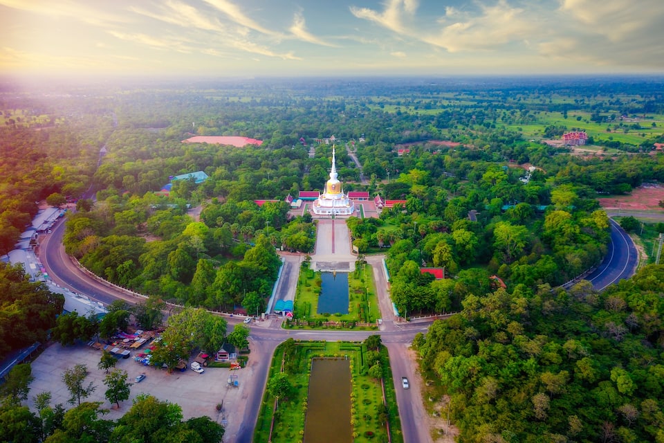 An aerial view of a temple complex surrounded by lush greenery, with a large central stupa and a surrounding road.