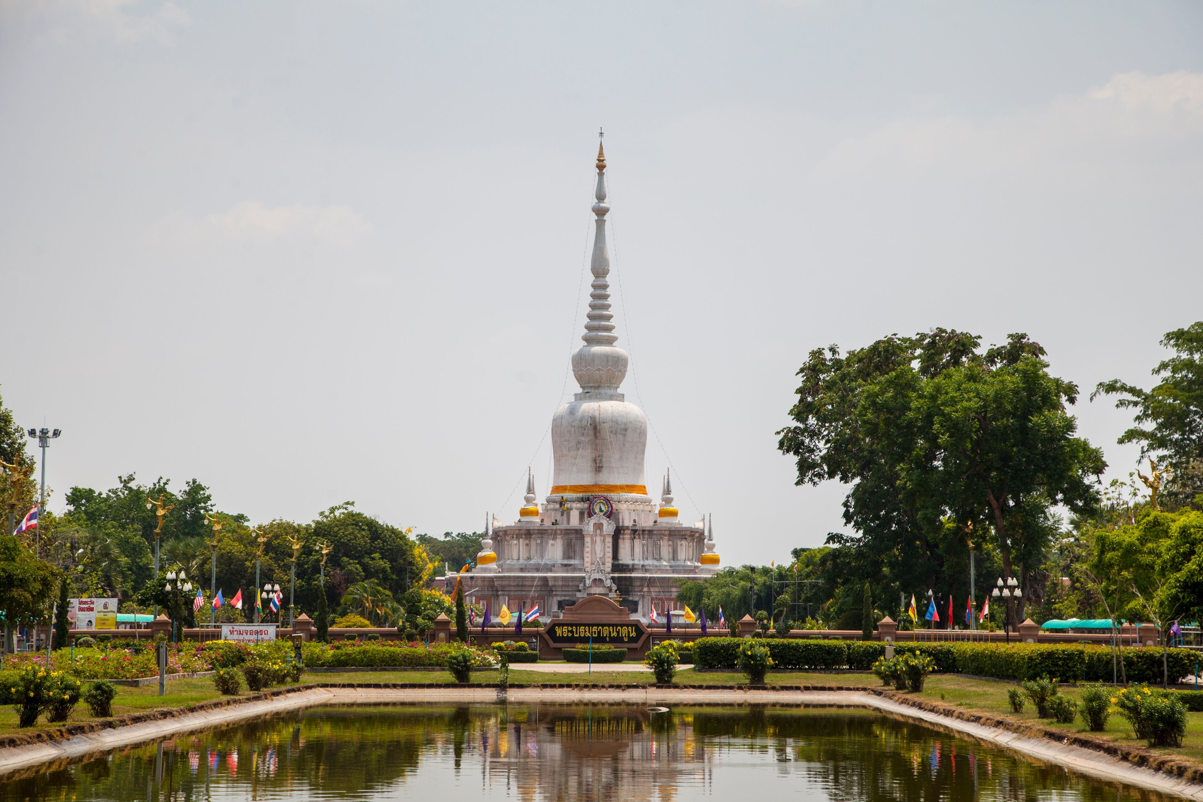 A large white stupa with a golden spire, surrounded by a reflective pond and lush greenery.
