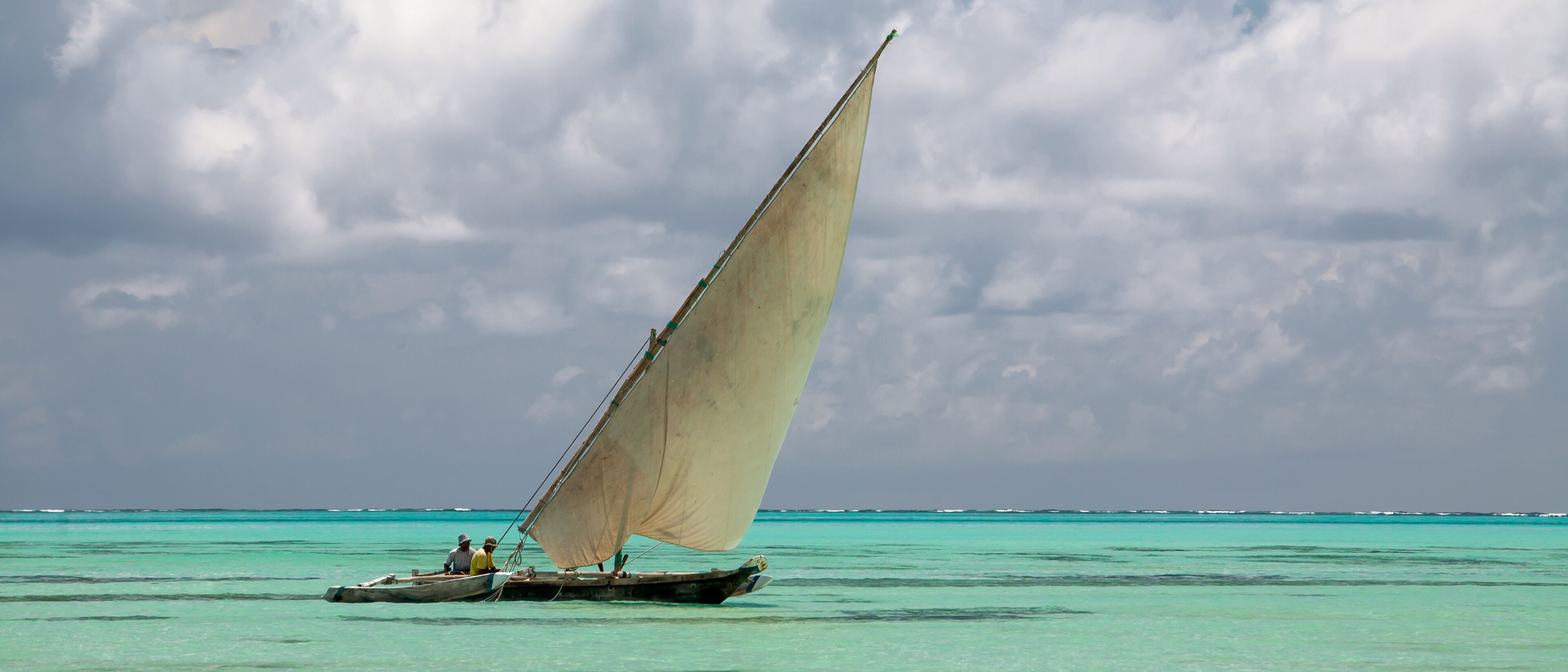 A sailboat with a large sail on turquoise waters under a cloudy sky.