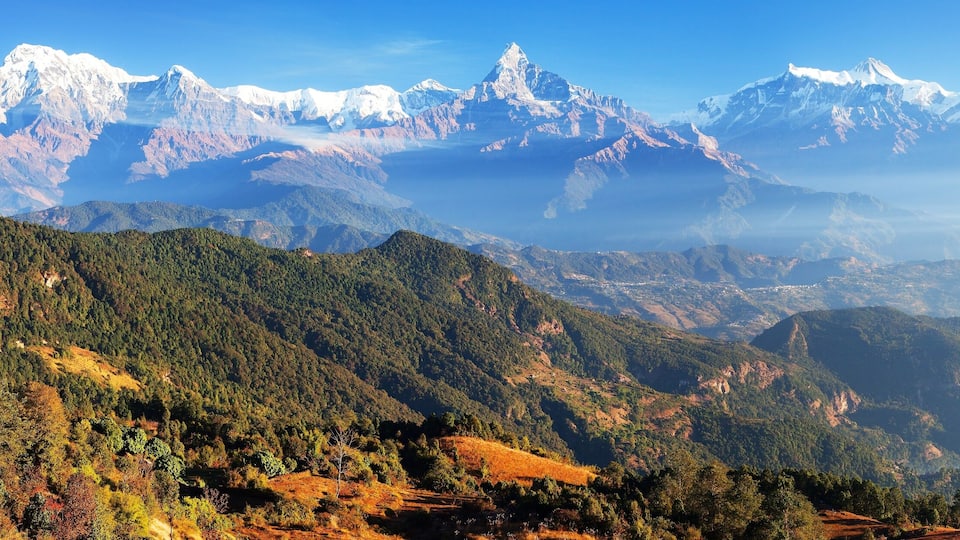 A mountainous landscape with snow-capped peaks and dense forested valleys.