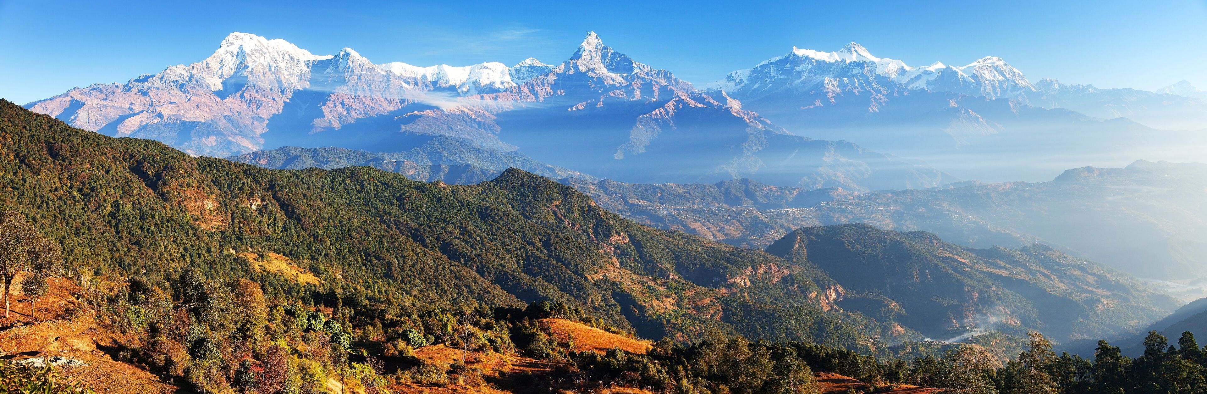 A mountainous landscape with snow-capped peaks and dense forested valleys.