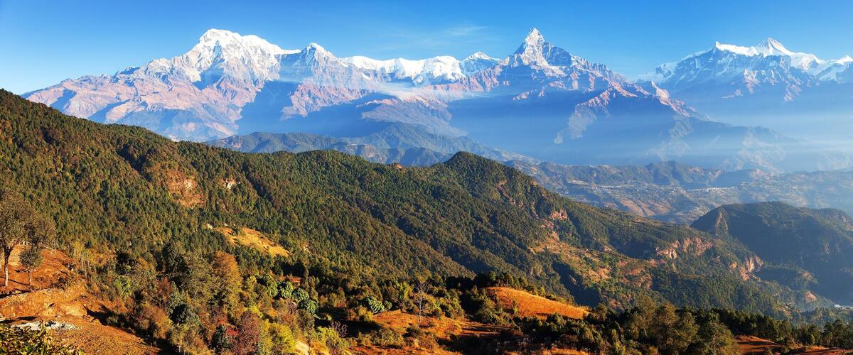 A mountainous landscape with snow-capped peaks and dense forested valleys.