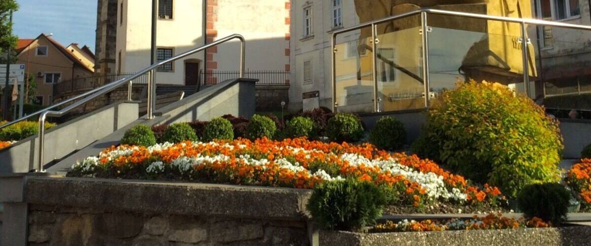 A church tower with a clock, a statue, and flower beds.