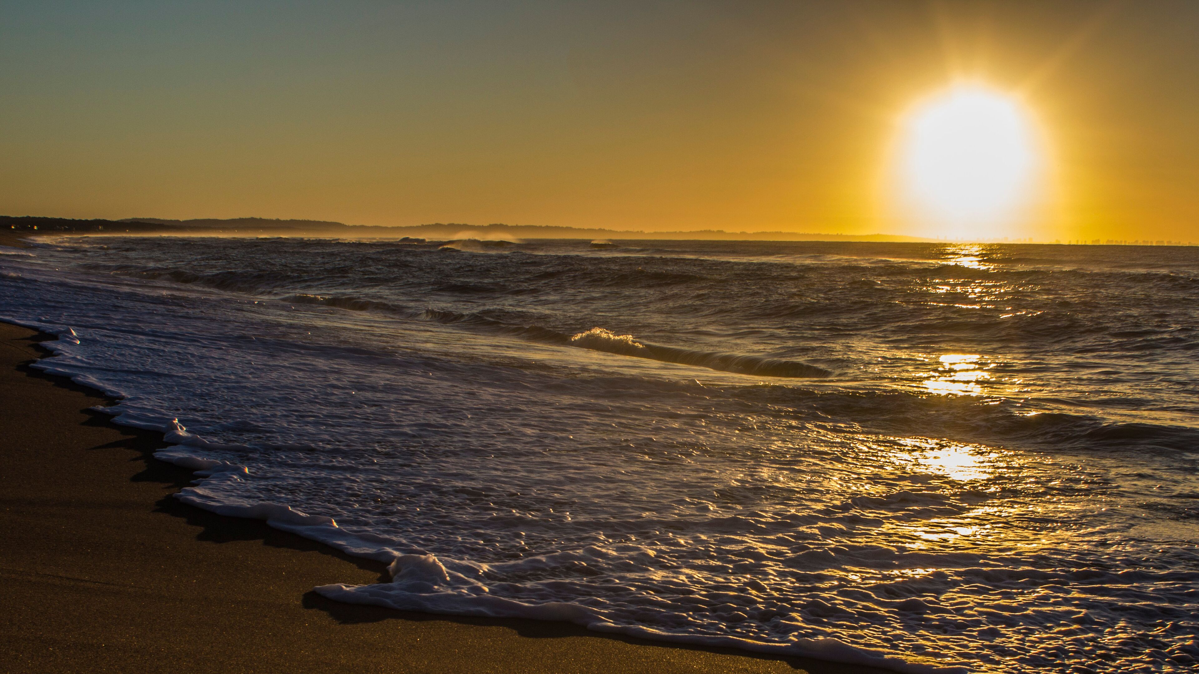 A beach with waves and a setting sun.