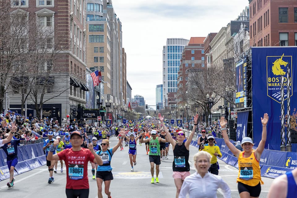 A marathon with runners on a city street lined with buildings and flags.