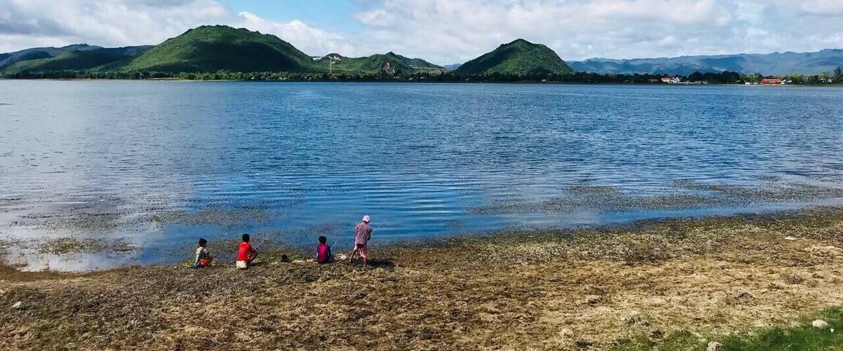 A lake with mountains in the background and four people on the shore.