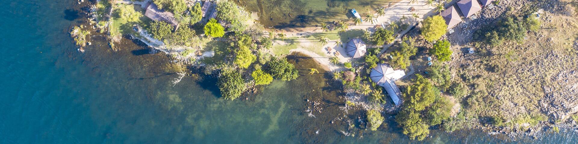 Aerial view of the island's rugged coastline meets the tranquil turquoise waters, fringed by lush vegetation and quaint structures, Takawiri Island, Homa Bay, Kenya.