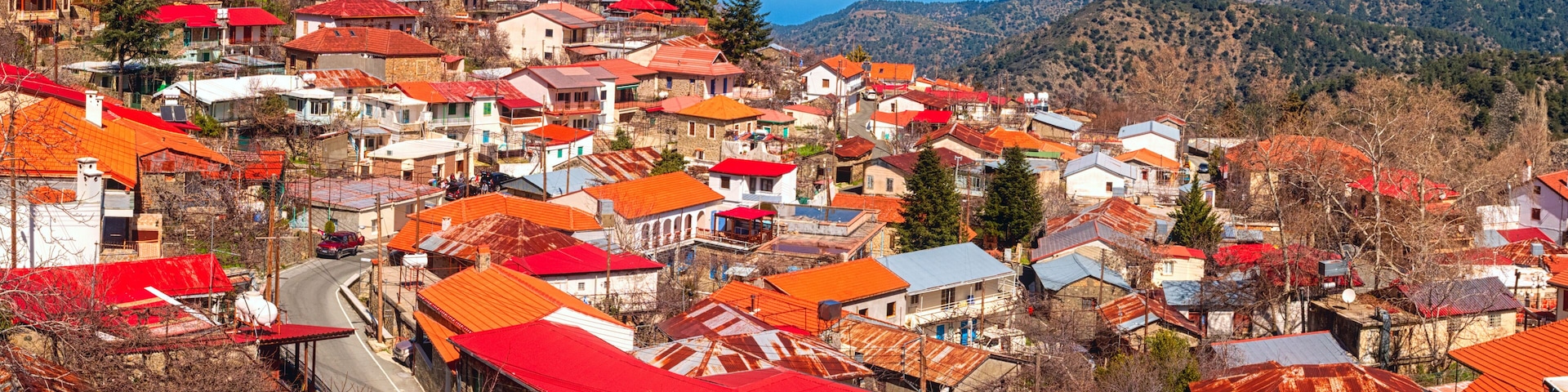 A town with red-roofed buildings, a clear blue sky, and mountains in the background.