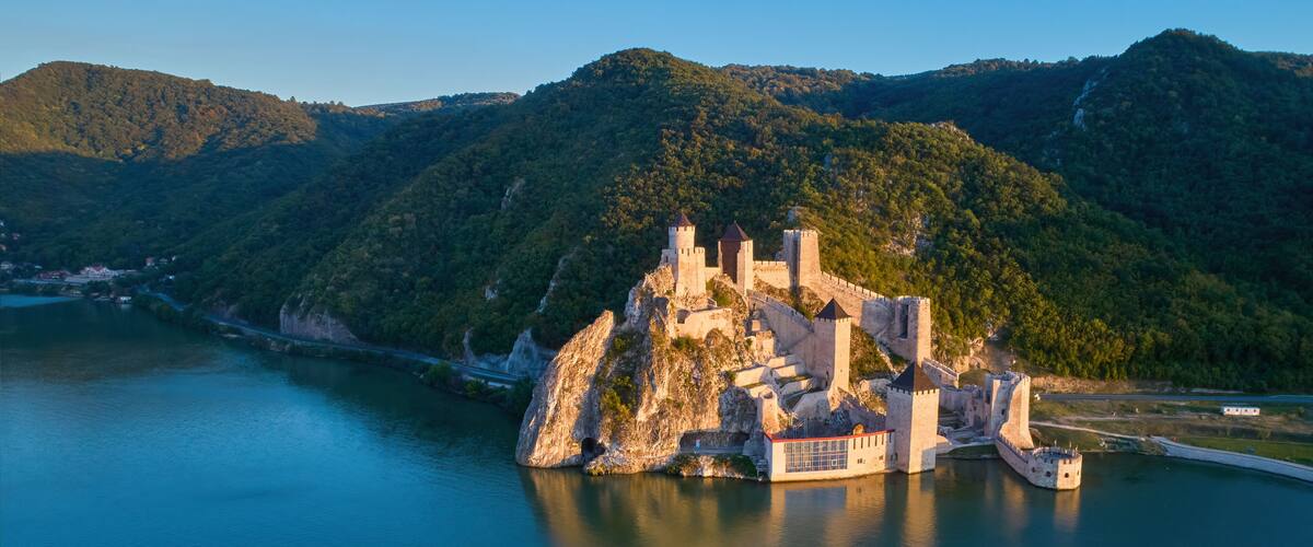 A medieval castle on a rocky island surrounded by a calm lake and forested hills.