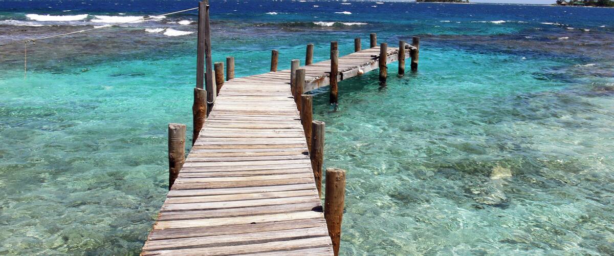 A wooden pier extending into clear turquoise waters with a distant island visible on the horizon.