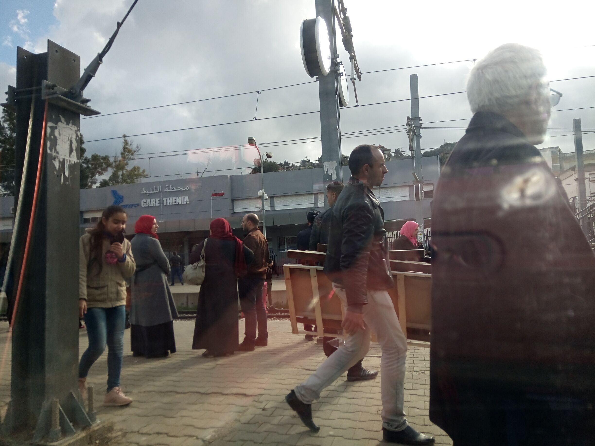 People walking on a paved area with a building labeled "GARE THENIA" in the background.