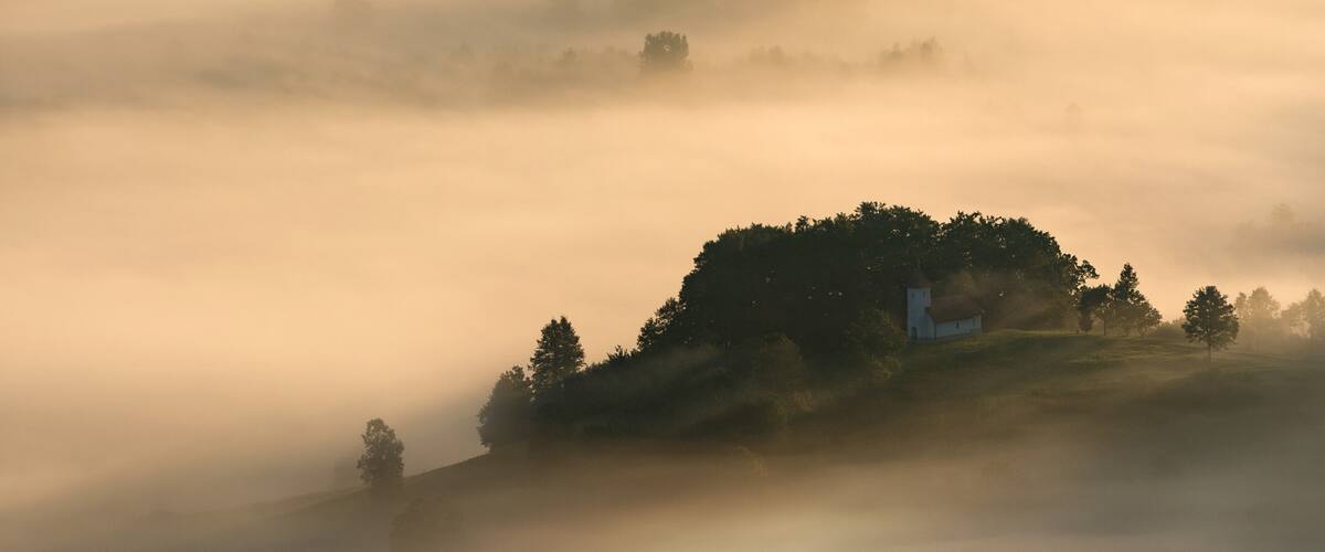 A misty landscape with a hill and a white building.
