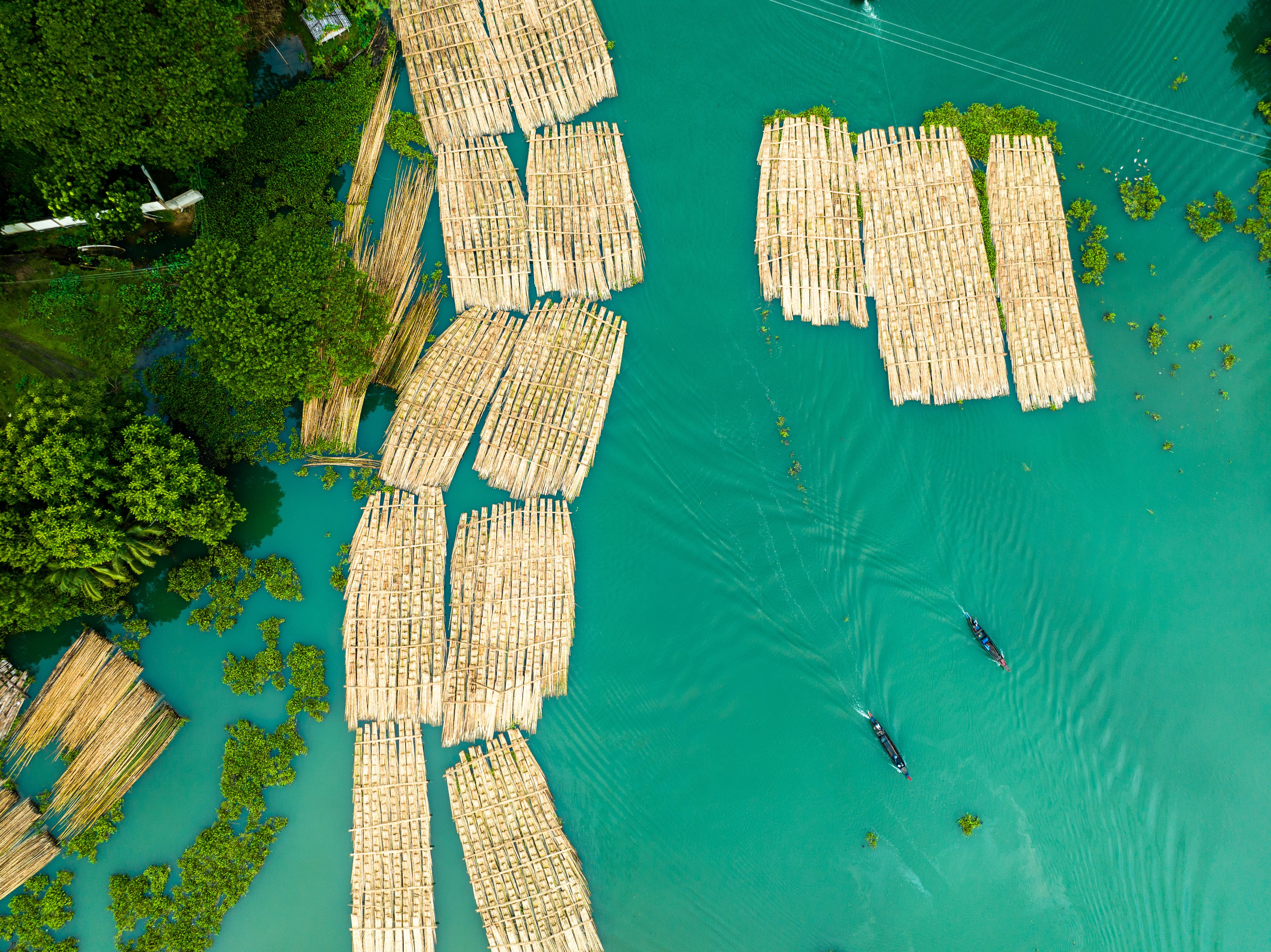 Vue aérienne d’un système de radeaux flottants en bambou sur une étendue d’eau turquoise, entourée d’une végétation luxuriante.